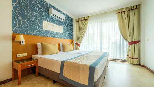 Hotelværelse med dobbeltseng, blå og guldfarvet indretning samt vindue med lyse gardiner. (AI-genereret tekst)