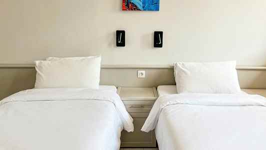 To enkeltsenge med hvidt sengetøj og et fælles natbord mellem dem. (AI-genereret tekst)