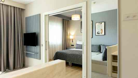 Billede af et hotelværelse med seng, spejl og tv. (AI-genereret tekst)