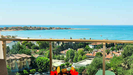 Udsigt fra en balkon over havet og bebyggelse med træer og bygninger. (AI-genereret tekst)