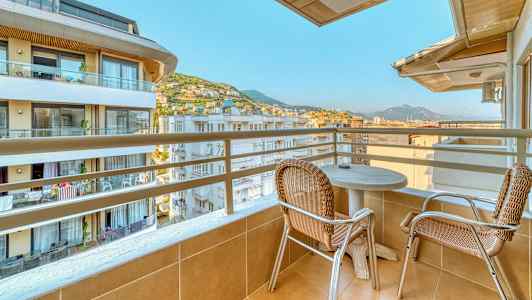 Altan med to stole og et bord, med udsigt over bygninger og bjerge. (AI-genereret tekst)