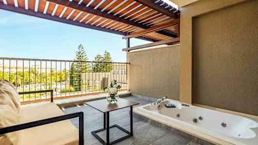 En terrasse med jacuzzi, siddemøbler, blomsterbuket og udsigt til grønne områder. (AI-genereret tekst)