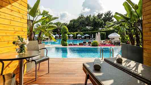 Terrasse foran en pool med liggestole, bord og planter. (AI-genereret tekst)