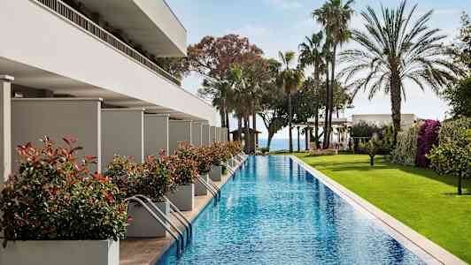 Lang pool omgivet af grønne områder og moderne bygninger. (AI-genereret tekst)