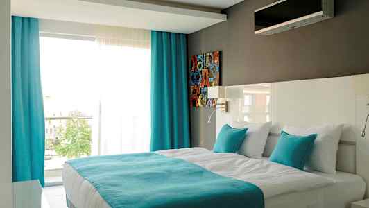 Moderne hotelværelse med en dobbeltseng, hvide og turkise farver. (AI-genereret tekst)