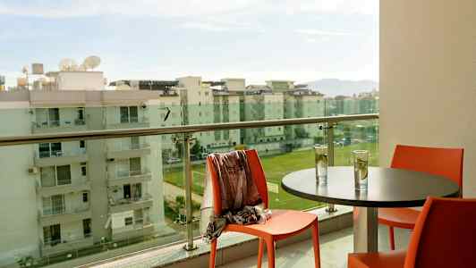 En altan med siddepladser, et bord med to glas og en udsigt over hotelbygninger. (AI-genereret tekst)