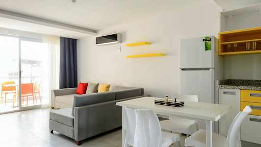 En stue med grå sofa, farverige puder, spisebord med stole og en åben altan. (AI-genereret tekst)