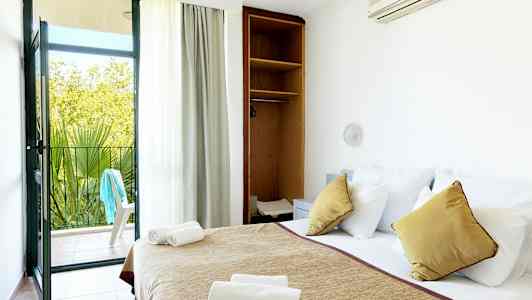 Et hotelværelse med en redt seng, åbent skab og en altandør, der fører ud til en terrasse. (AI-genereret tekst)