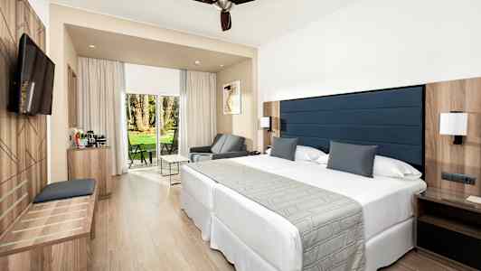 Et hotelværelse med en dobbeltseng, siddeområde og en terrasse med udsigt over en have. (AI-genereret tekst)