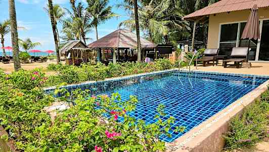 En pool med blå fliser omgivet af haveplanter og tropiske palmer. (AI-genereret tekst)