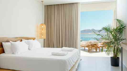 Et lyst soveværelse med dobbeltseng og udsigt over havet. (AI-genereret tekst)