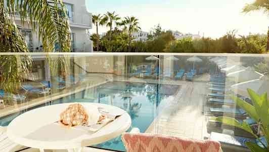 Udsigt fra en terrasse der viser en pool med solsenge og parasoller omgivet af grønne områder. (AI-genereret tekst)