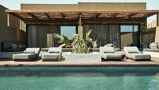 Billede af en pool foran en terrasse med liggestole og sofagruppe. (AI-genereret tekst)