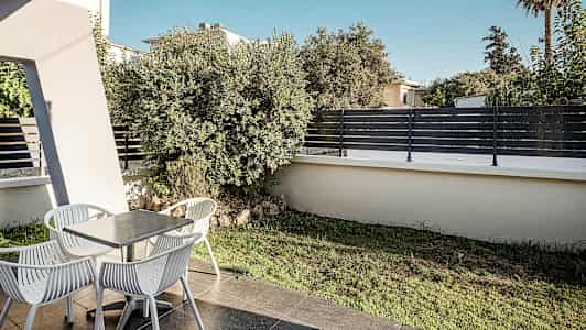 En terrasse med et bord og fire stole, omgivet af bevoksning og hegn. (AI-genereret tekst)