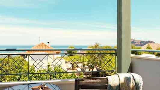 Udsigt fra en balkon med et glasbord og stol. Havet og huse ses i baggrunden. (AI-genereret tekst)