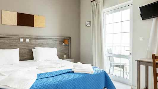 Et hotelværelse med en dobbeltseng, blåt sengetæppe og hvidt sengetøj. (AI-genereret tekst)