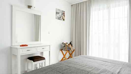 Et lyst soveværelse med et spejl, bord og en stol ved vinduet med gardiner. (AI-genereret tekst)