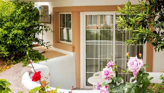 Indgang med hvid facade og en terrasse dekoreret med roser og grønt. (AI-genereret tekst)