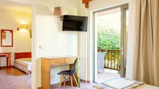 Et hotelværelse med skrivebord, stol, TV og altan med udendørs møbler. (AI-genereret tekst)