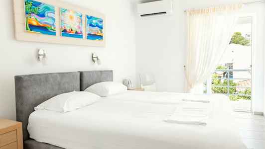 Et lyst hotelværelse med en dobbeltseng, kunstværk på væggen og et åbent vindue med udsigt. (AI-genereret tekst)