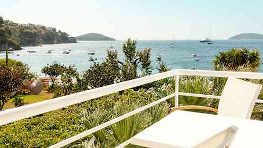 Udsigt fra en altan over havet med både og vegetation. (AI-genereret tekst)