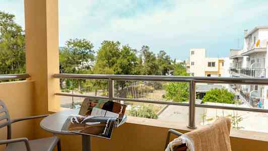 Altan med udsigt over grønne områder og bygninger, et bord med en magasin og to stole. (AI-genereret tekst)