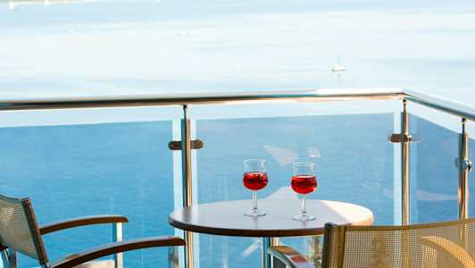 To glas med rød drik på et bord på en altan med udsigt over havet. (AI-genereret tekst)