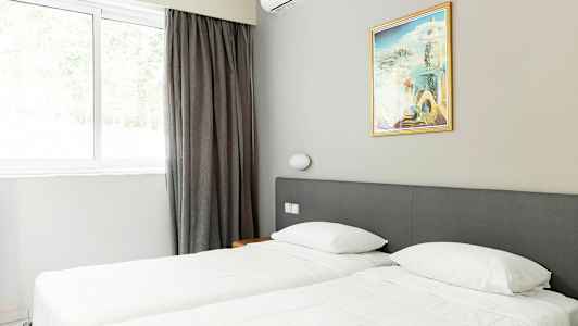 Et værelse med to enkeltsenge, et maleri og et vindue med gardiner. (AI-genereret tekst)