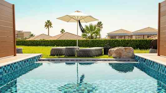 En swimmingpool med liggestole og en parasol i baggrunden. (AI-genereret tekst)