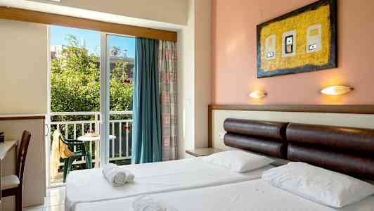 Et hotelværelse med dobbeltseng, sengelamper, skrivebord og en balkon med udsigt til grønne omgivelser. (AI-genereret tekst)