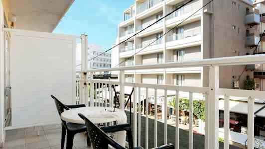 En altan med to stole og et bord, udsigt til bygninger. (AI-genereret tekst)