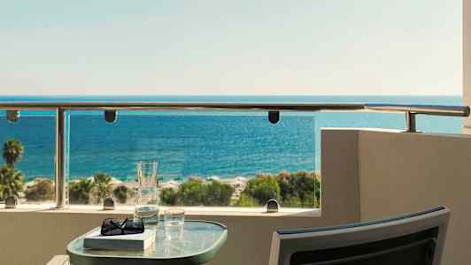 Udsigt over havet fra en balkon med et bord med glas og bog placeret på. (AI-genereret tekst)