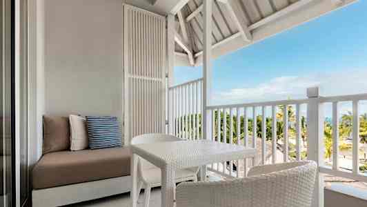 Møbler på en åben balkon med udsigt til palmer og hav. (AI-genereret tekst)