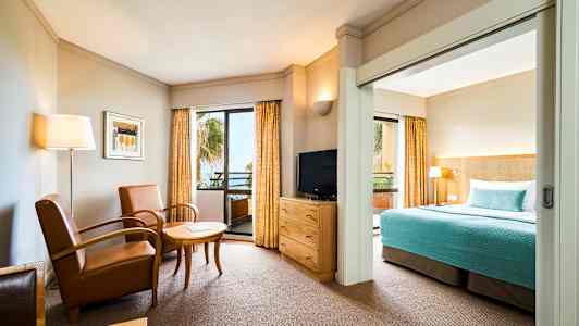 Et hotelværelse med siddeområde, tv og seng med blåt sengetæppe. (AI-genereret tekst)