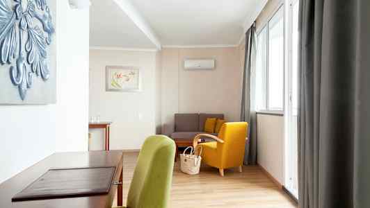 Et velindrettet opholdsrum med en grøn og en gul stol, en sofa og et skrivebord. (AI-genereret tekst)