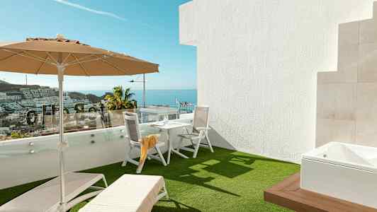 Terrasse med solsenge, parasol og bord med stole, havudsigt i baggrunden. (AI-genereret tekst)