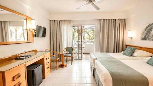 Hotelværelse med to senge, et skrivebord, en fladskærms-TV og en altan med udsigt. (AI-genereret tekst)