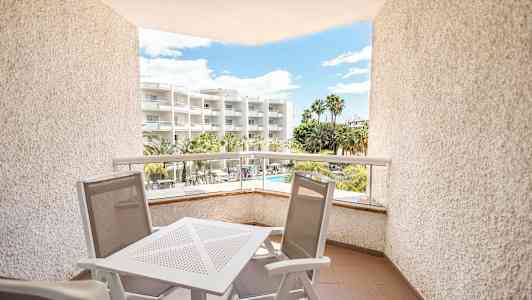 En altan med havemøbler, udsigt til et hotel med palmer og pool. (AI-genereret tekst)