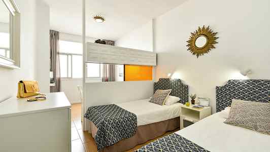 Et hotelværelse med to enkeltsenge dekoreret med mønstrede overkast og puder, hvide vægge og et spejl på væggen. (AI-genereret tekst)