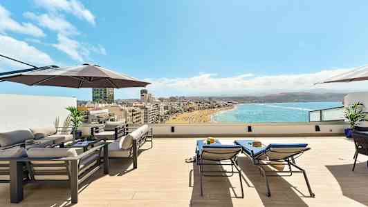 Tagterrasse med møbler, parasoller og udsigt over en strand og havet. (AI-genereret tekst)