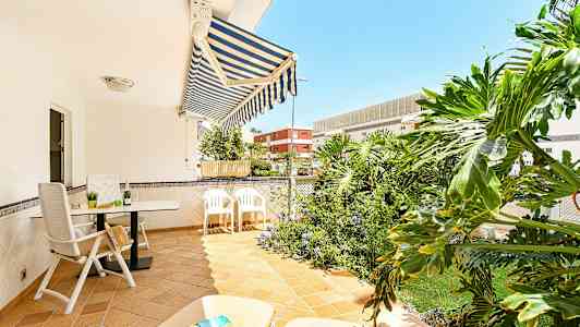 En terrasse med havemøbler, markise og grønne planter i baggrunden. (AI-genereret tekst)