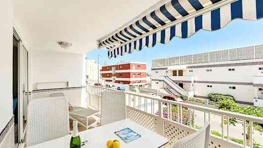 En altan med møbler, parasol og udsigt til bygninger. (AI-genereret tekst)