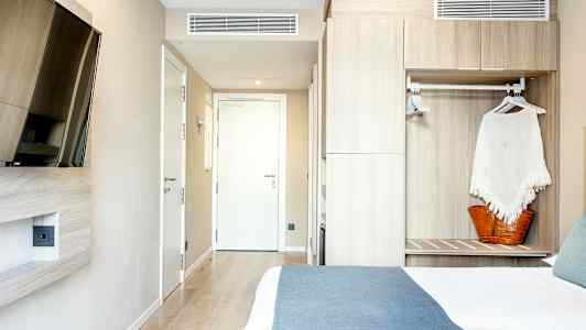 Et hotelværelse med en seng, et vægmonteret tv og et skab. (AI-genereret tekst)