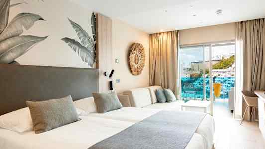 Et moderne hotelværelse med to senge, lyst interiør og en balkon med udsigt til en pool og bygninger. (AI-genereret tekst)