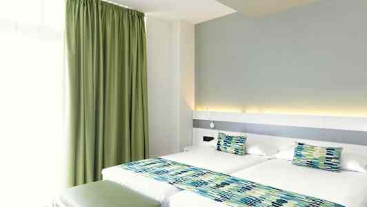 Et hotelværelse med to enkeltsenge, grønne gardiner og matchende sengedekorationer. (AI-genereret tekst)