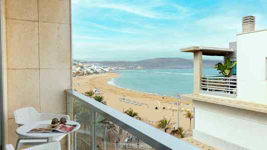 En altan med bord og stole giver udsigt over en sandstrand og havet. (AI-genereret tekst)