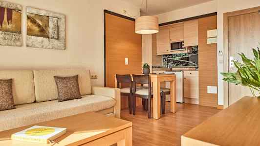 Billede af et moderne hotelværelse med en lys sofa, et bord med stole og et hjørnekøkken. (AI-genereret tekst)