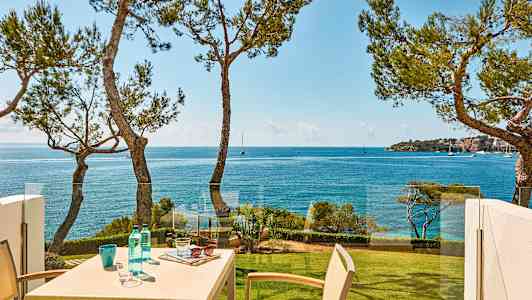 En udsigt over havet med et bord på en balkon omgivet af træer. (AI-genereret tekst)