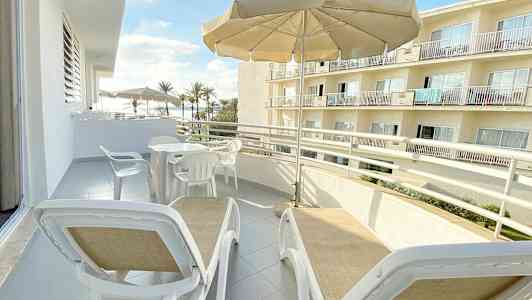 Altan med liggestole under en parasol og udsigt til bygninger og palmer. (AI-genereret tekst)