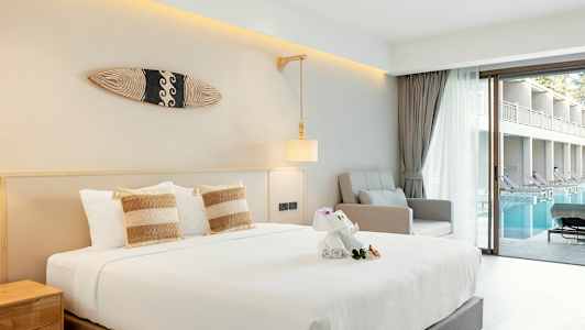 Hotelværelse med seng, lænestol og udsigt over pool fra en glasdør. (AI-genereret tekst)